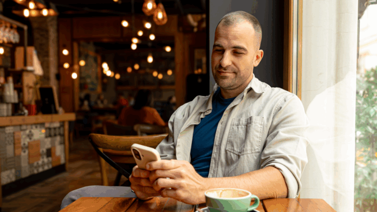 Man sipping cappuccino while browsing social media on a smartphone, enjoying a relaxed morning in a cosy café setting